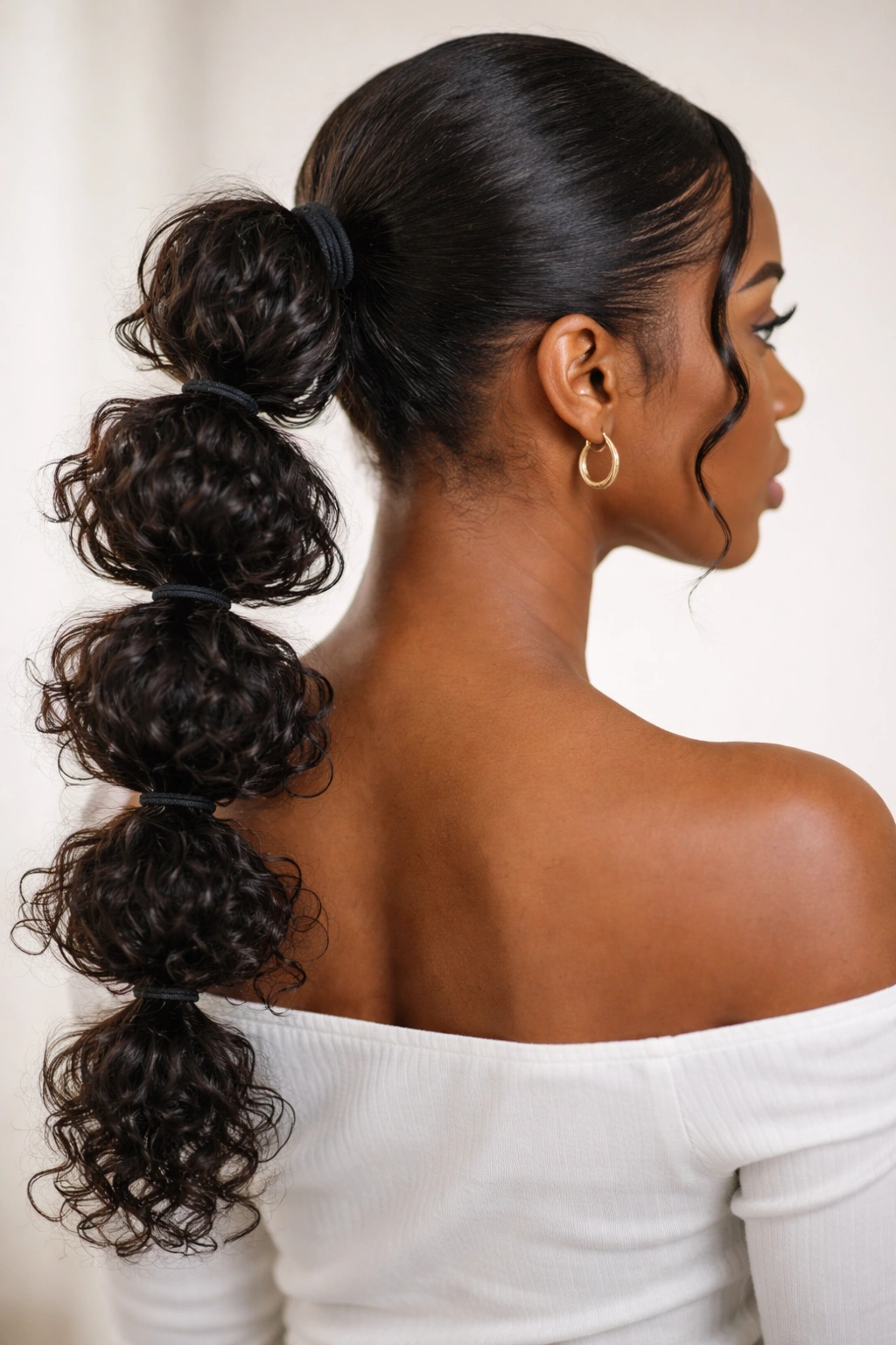 Low bubble ponytail with curly sections visible between elastic bands.