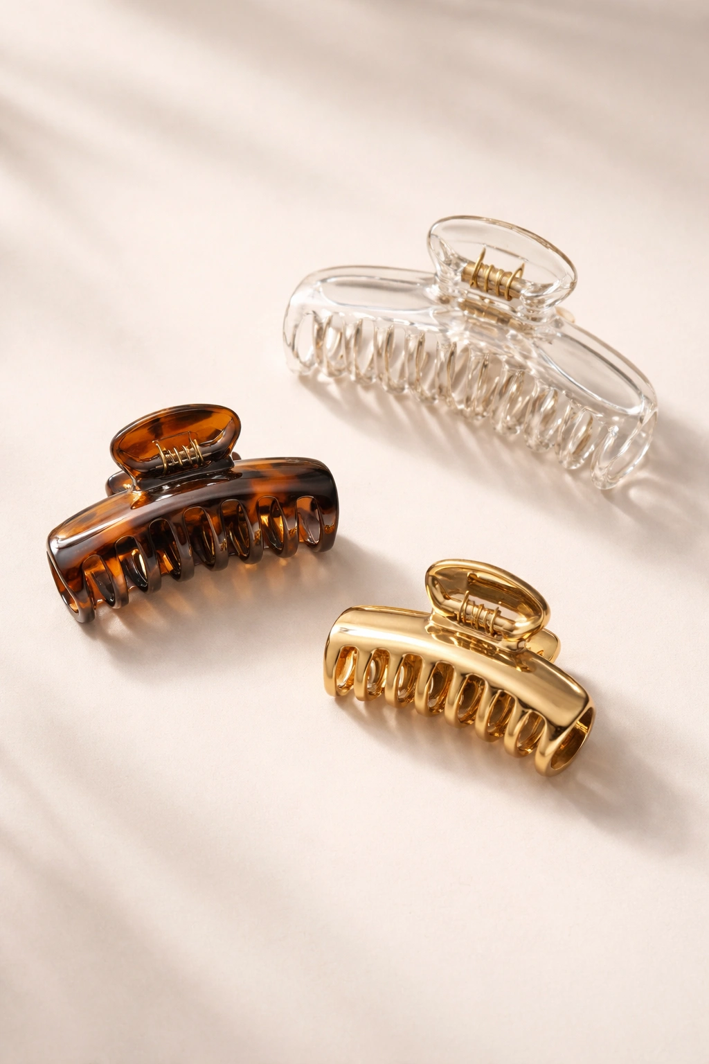Close-up of three claw clips in different sizes and finishes on a neutral surface