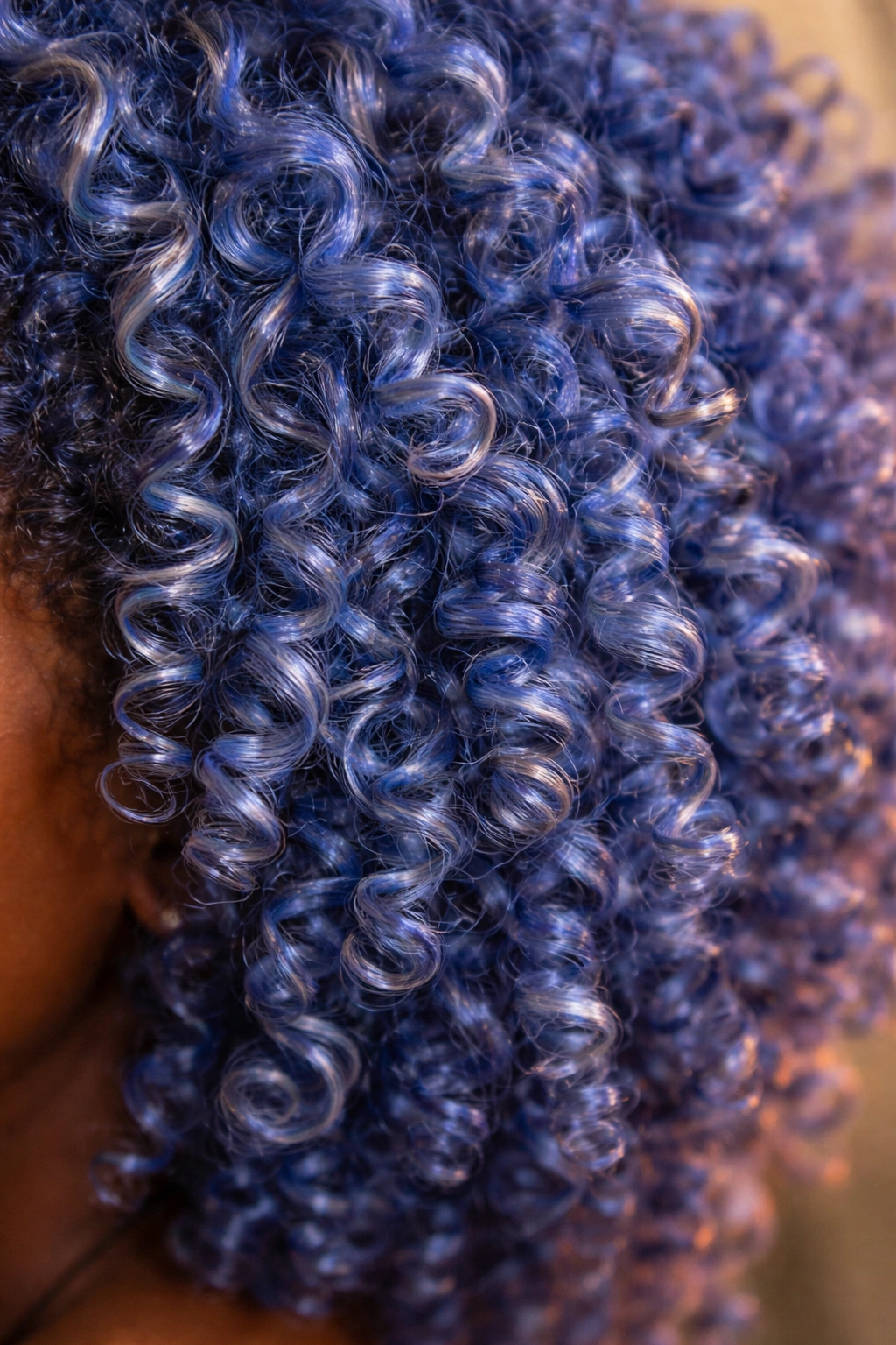Coily hair in cornflower blue with warm undertones catching jewel-like light