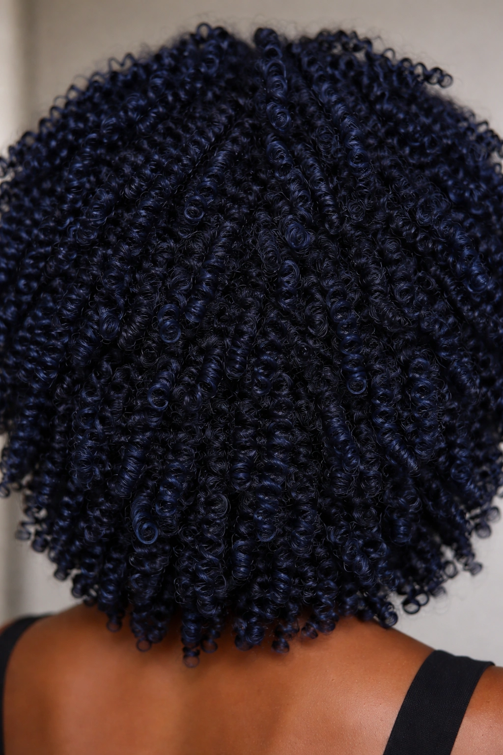 Close-up of deep navy blue coily hair with defined curls and dimensional shading