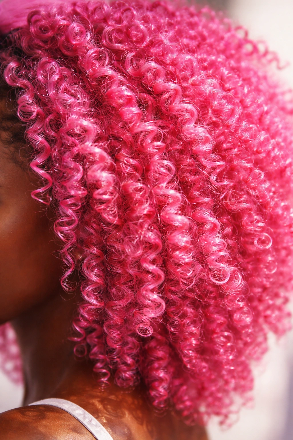Close-up of coily hair in hot pink with bright reflections on the curl texture