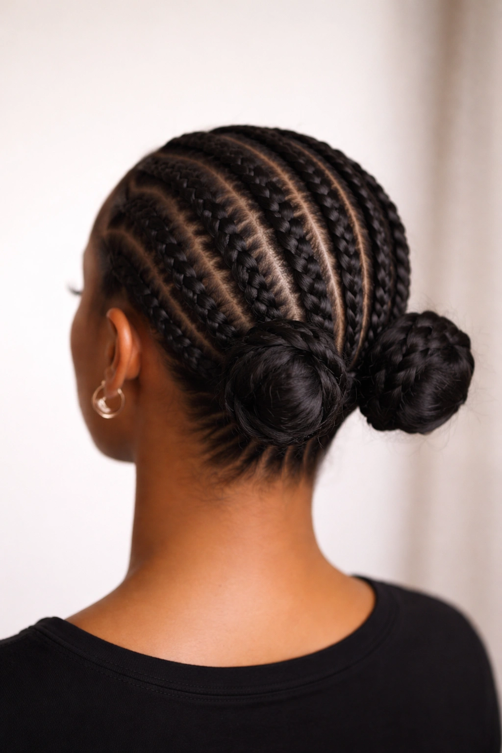 Back view of low space buns created from feed-in cornrows at the nape, conveying an understated professional hairstyle