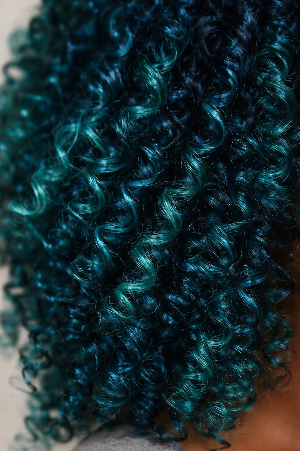 Close-up of teal blue-green coily hair showing color shifts and curl depth