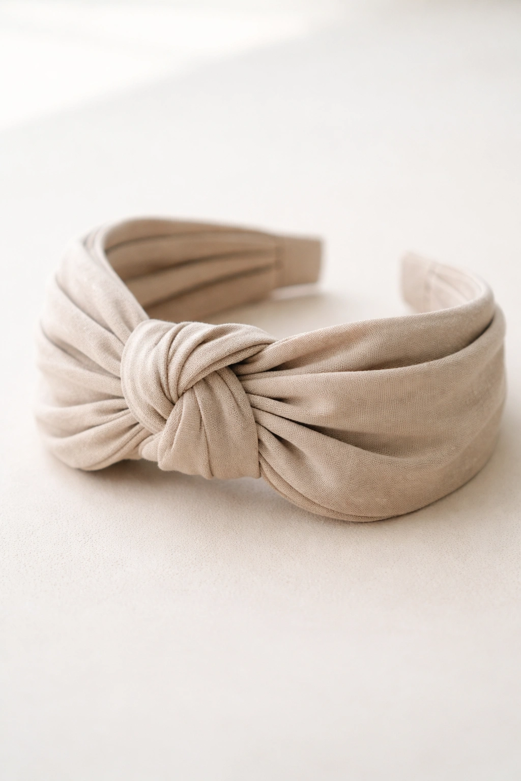 Knotted fabric turban headband with front knot and wrapped fabric on neutral background