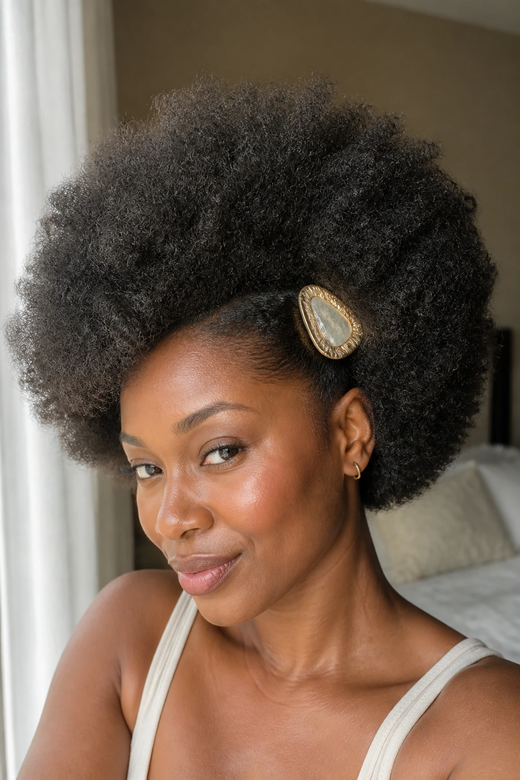 Close-up of a real woman's picked-out Afro with one statement clip above the ear in warm window light